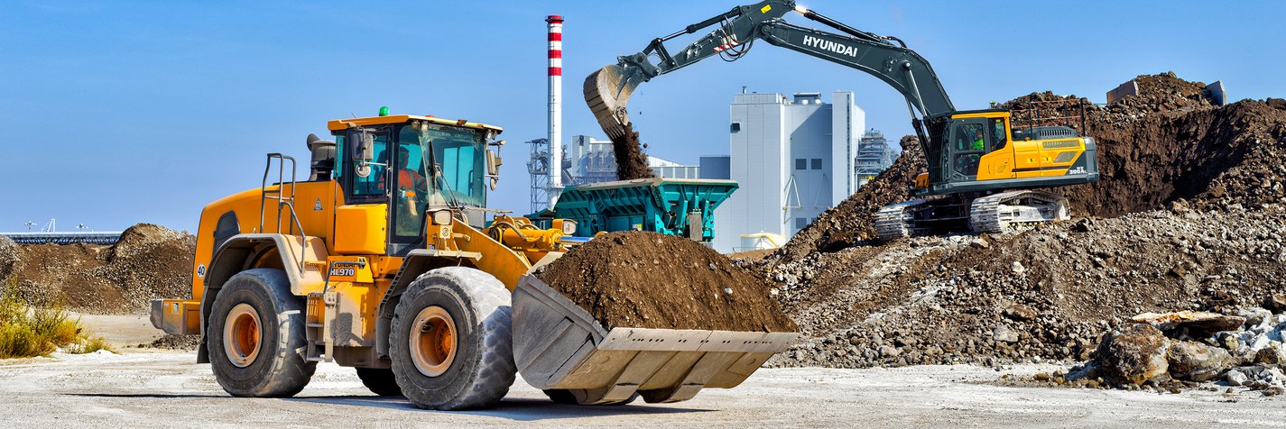 Telakoneen valikoimiin kuuluvat Hyundai-pyöräkuormaaja sekä tela-alustainen Hyundai-kaivinkone tekevät maanrakennustöitä työmaalla.